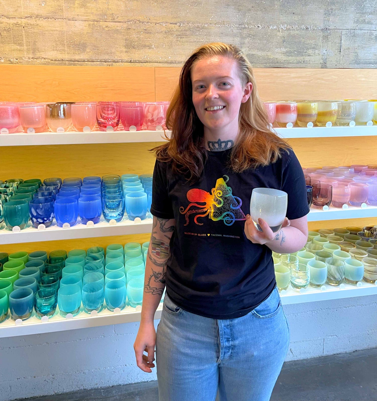 glassybaby glassblower, Karlie holding a votive in front of glassybaby retail shelves.