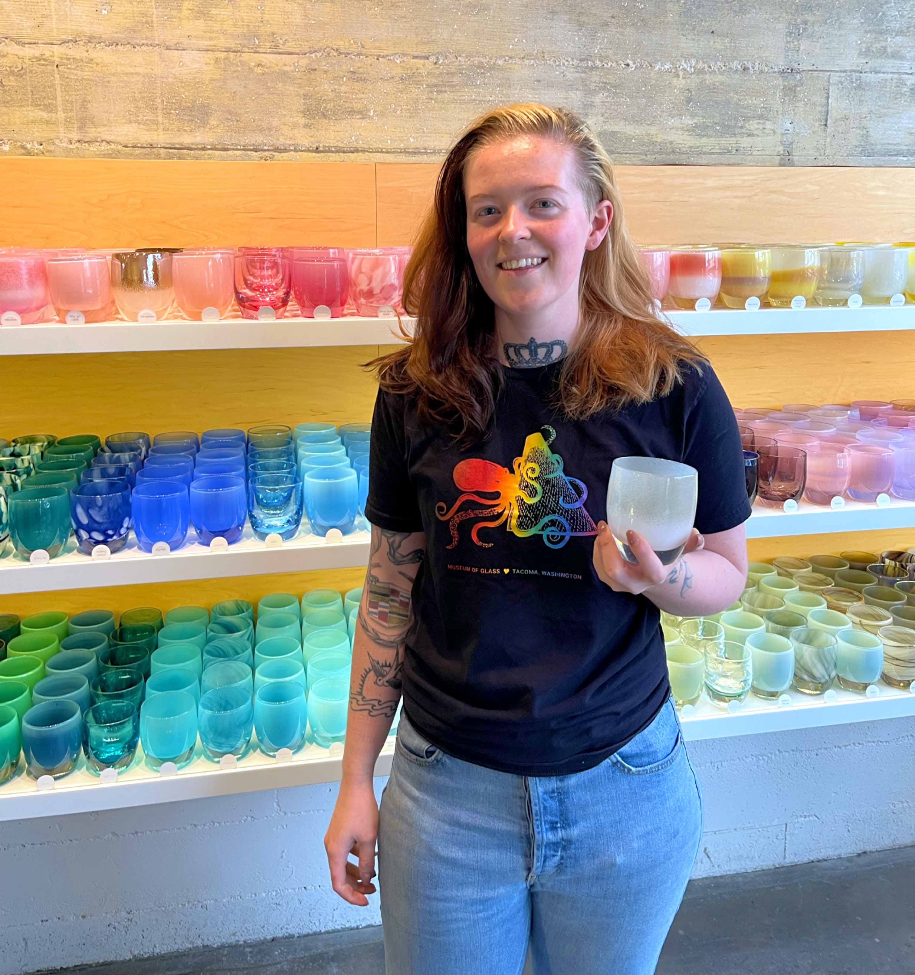 glassybaby glassblower, Karlie holding a votive in front of glassybaby retail shelves.