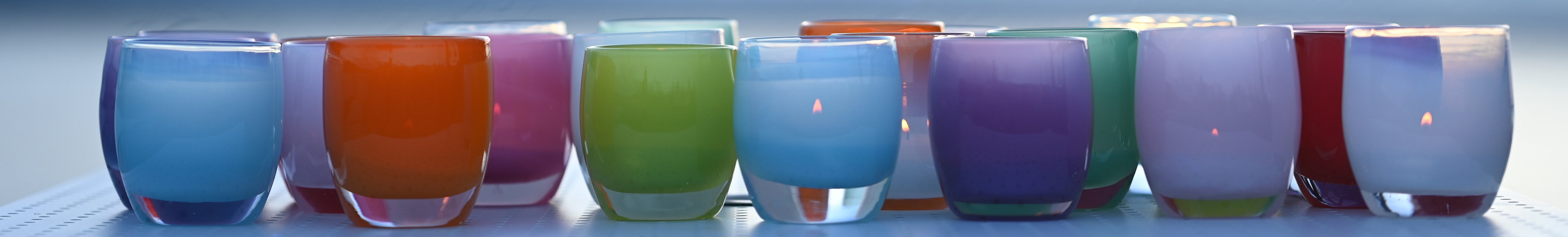 grouping of core, varying solid color hand-blown glass votive candle holders outside at sunset.