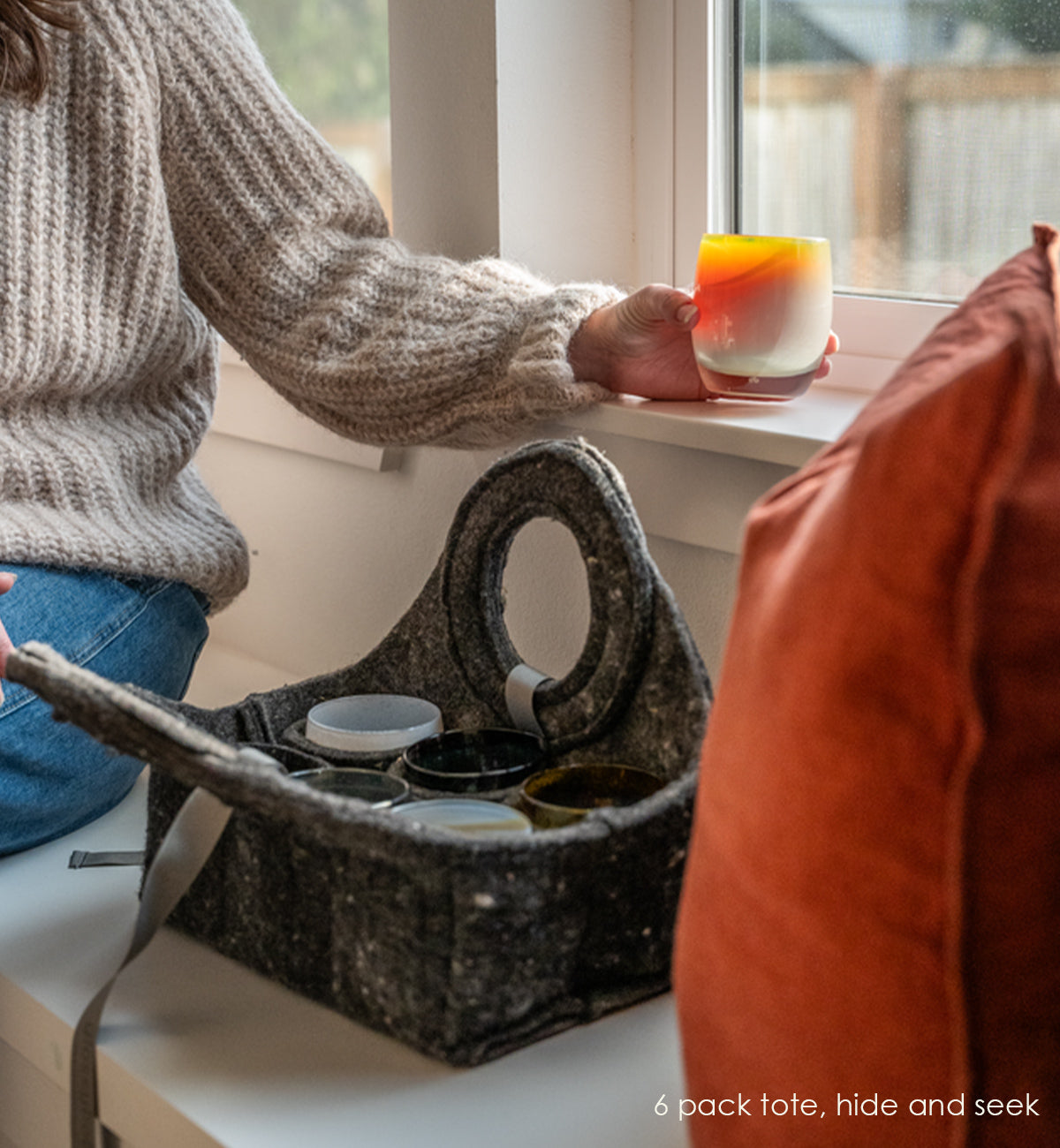 6 pack tote sitting on bench with someone pulling a hide and seek glassybaby from it and placing it on windowsill.