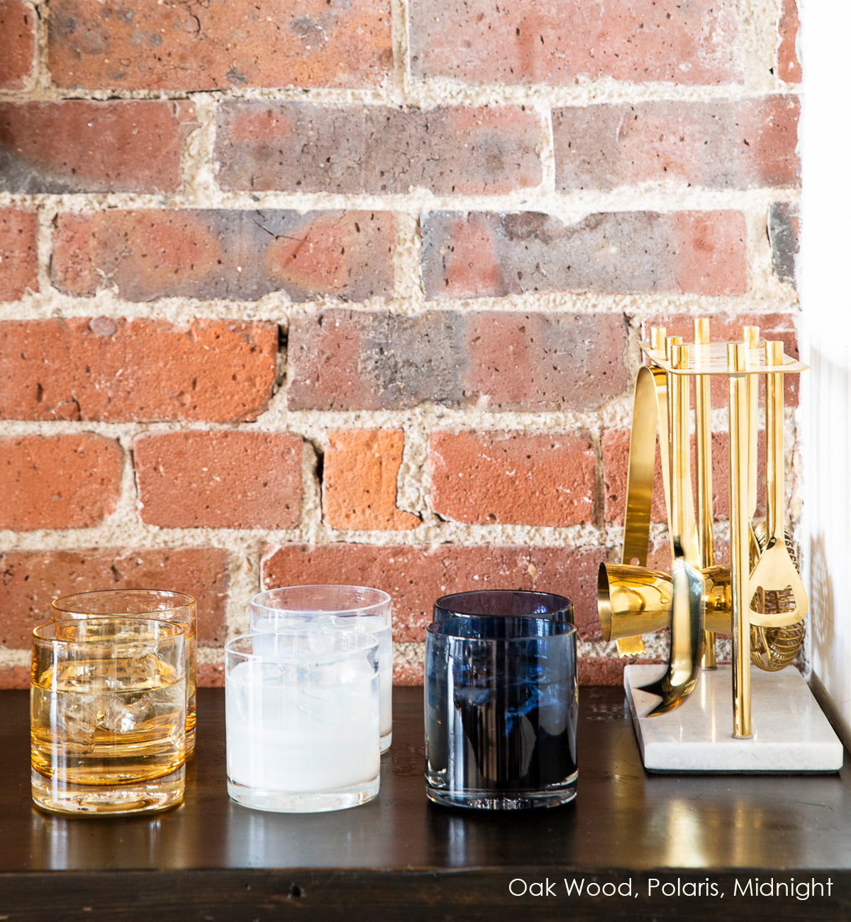 Oak Wood, Polaris, and Midnight rockers, white, light brown and dark blue hand-blown glass lowball drinking glasses sitting atop a dark wood table, with brick and bar ware in background.