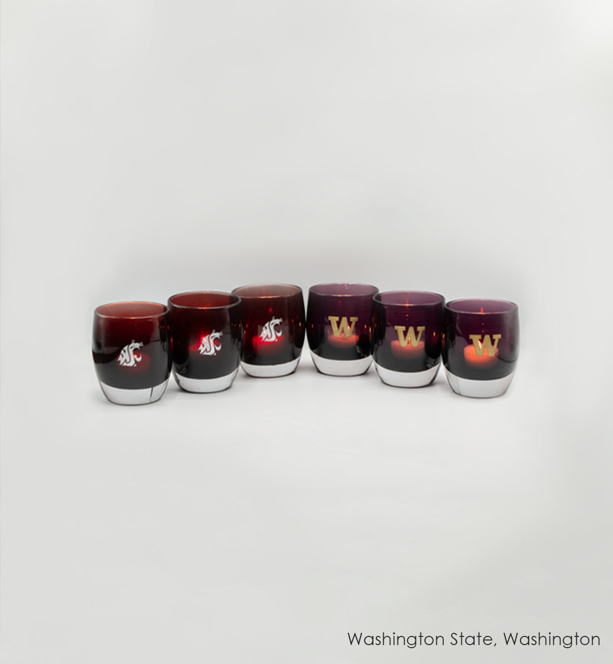 Washington State University and University of Washington hand-blown glass votives sitting in a row with a cream background.