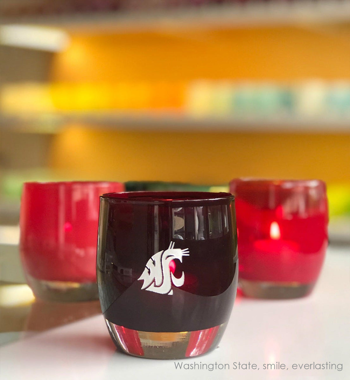 Washington State, crimson with sandblasted washington state university etching hand painted in silver, hand-blown glass votive candle holder. Paired with everlasting and smile on a white and clear table.