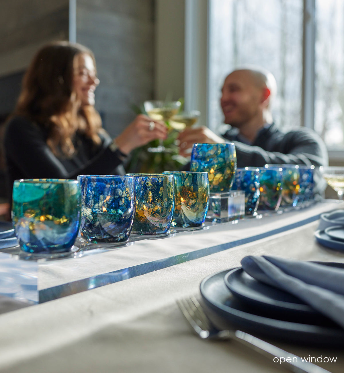 blue with transparent specs hand-blown glass candle holders on glass stand on dinner table with people drinking