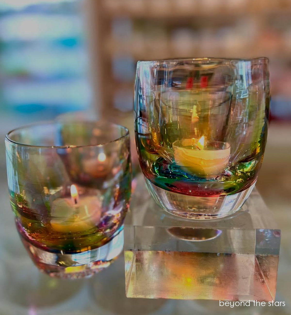 beyond the stars multicolor translucent, hand-blown glass votive candle holder. lit on glass stand.