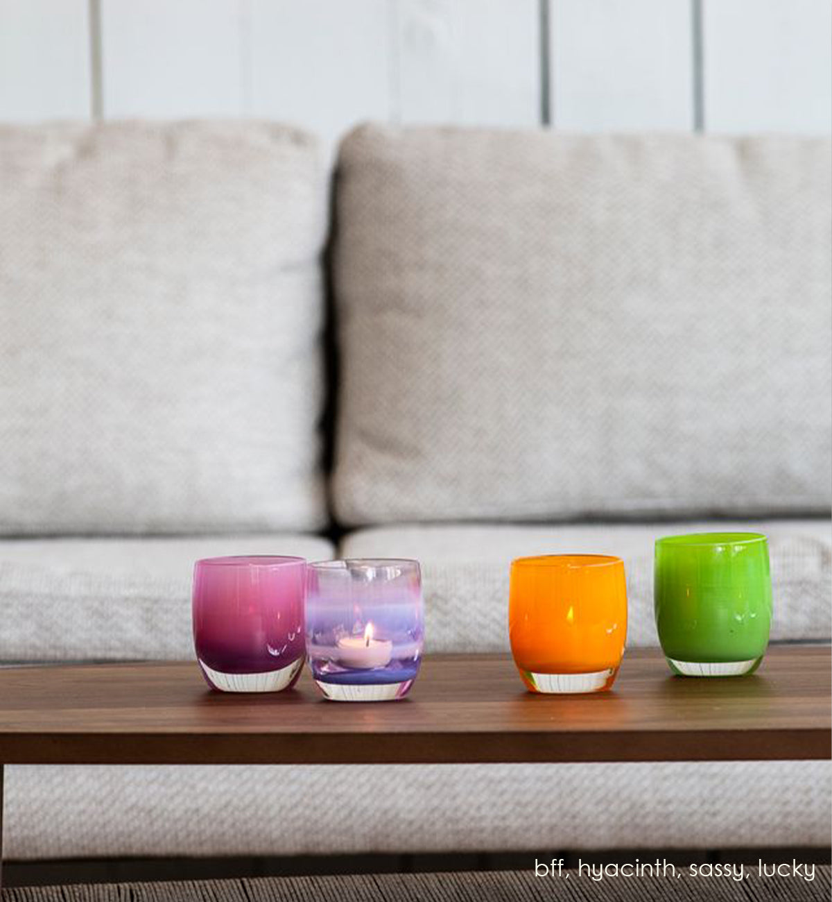 bff fuscia hand-blown glass votive candle holder on a coffee table with hyacinth, sassy and lucky in front of a plush gray couch.