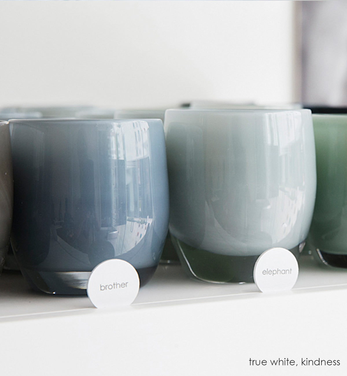 brother smokey gray hand-blown glass votive candle holder next to elephant on a glassybaby shelf.