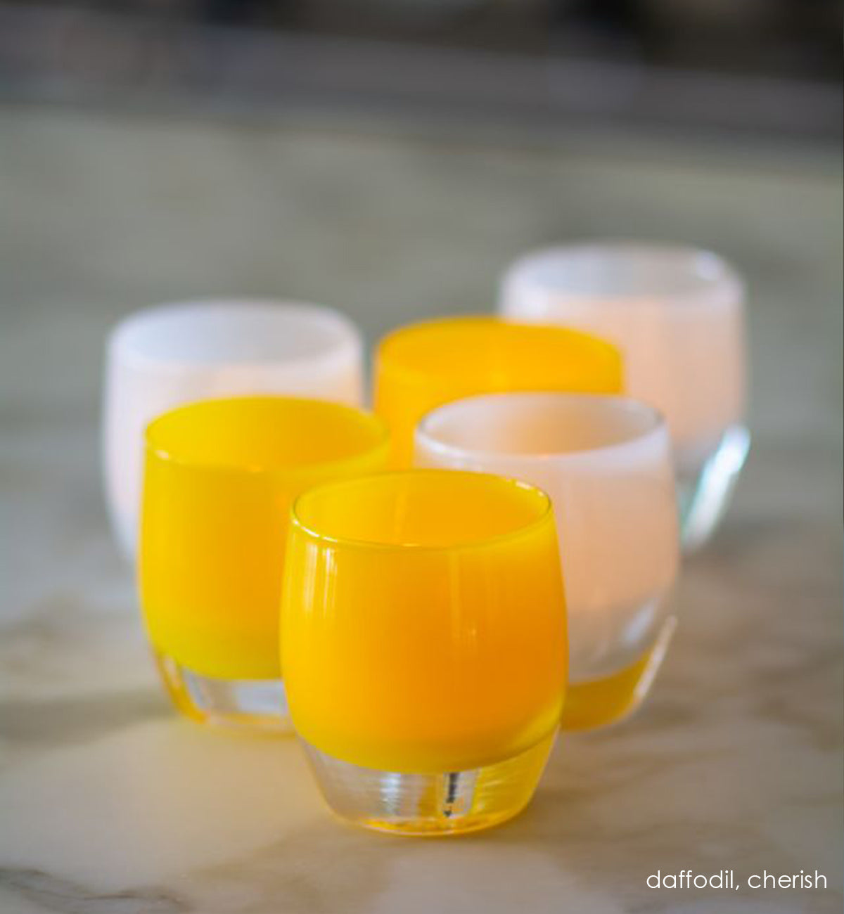 three daffodil opaque yellow hand-blown glass votive candle holders on a marble countertop with three chrerish.