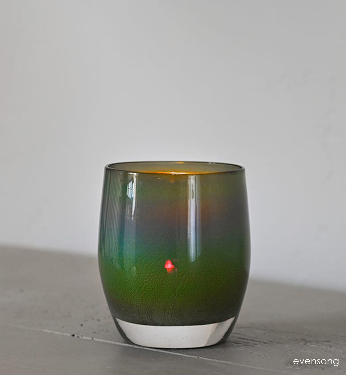 evensong hand-blown green, blue and brown glass votive candle holder on a gray wood surface with white background.