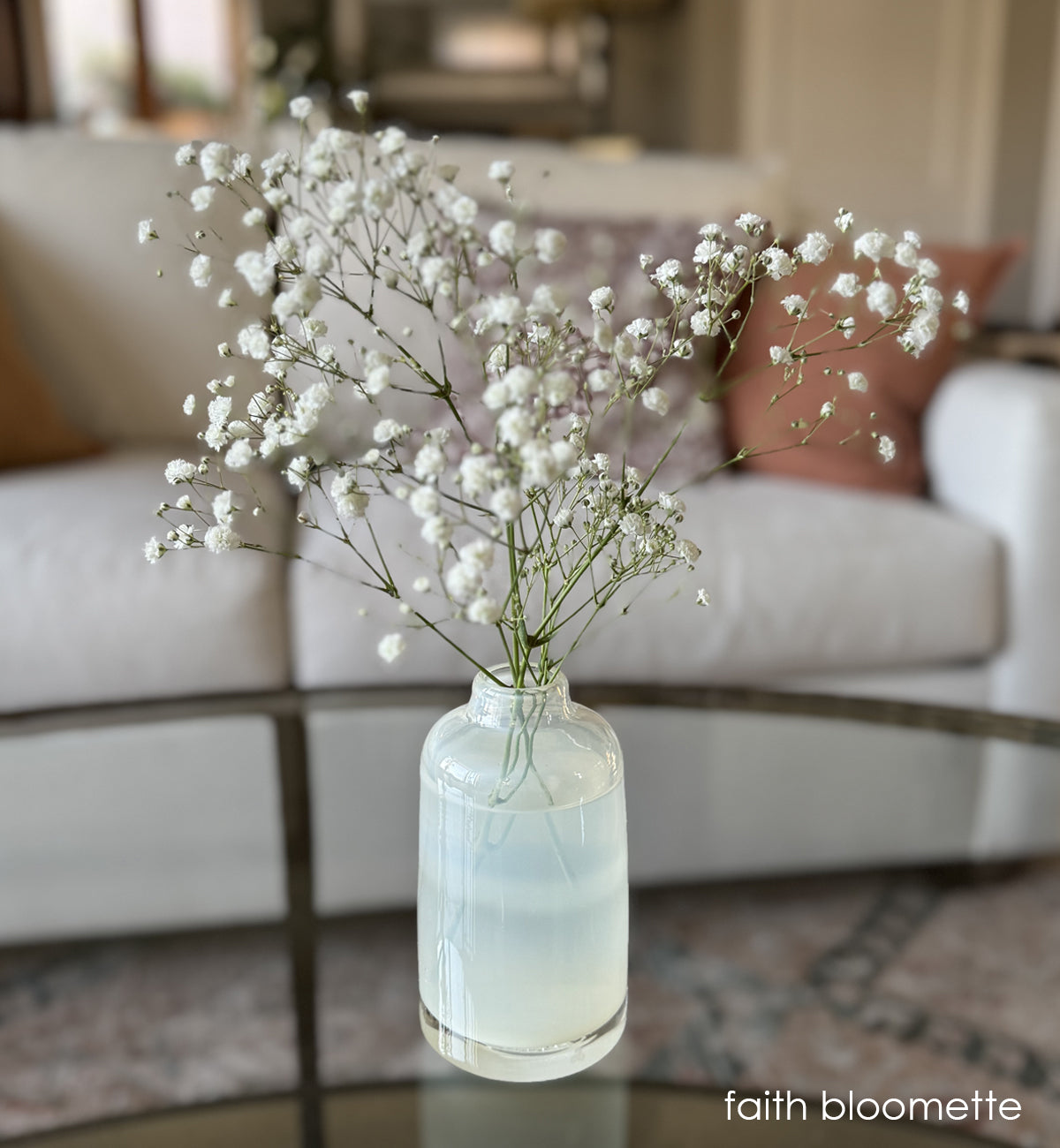 faith bloomette, translucent cream hand-blown glass flower bud vase with white flowers on glass table in a cream room.