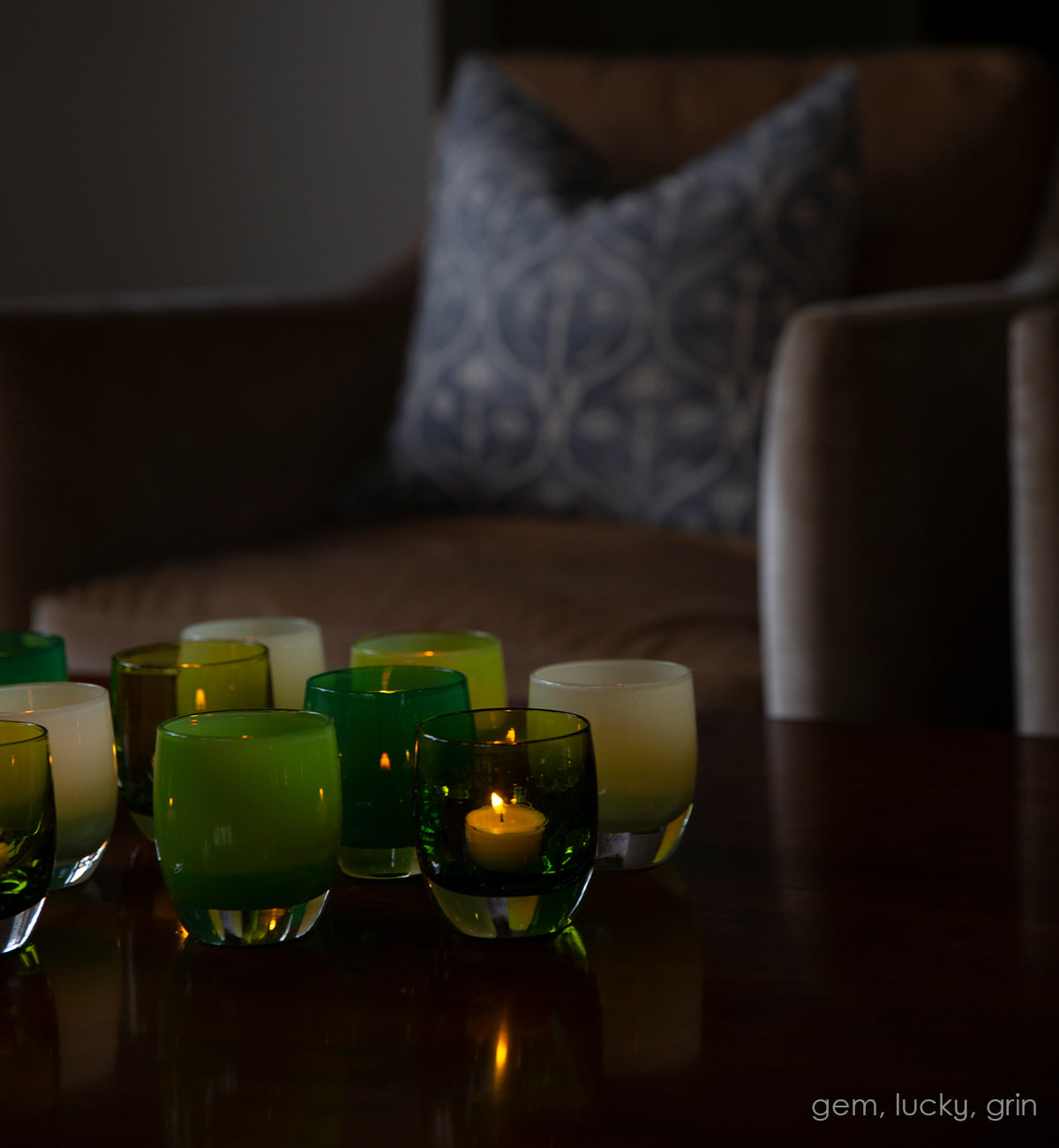 gem transparent green, hand-blown glass votive candle holder lit with a tealight in a dark room on a table with lucky and grin.