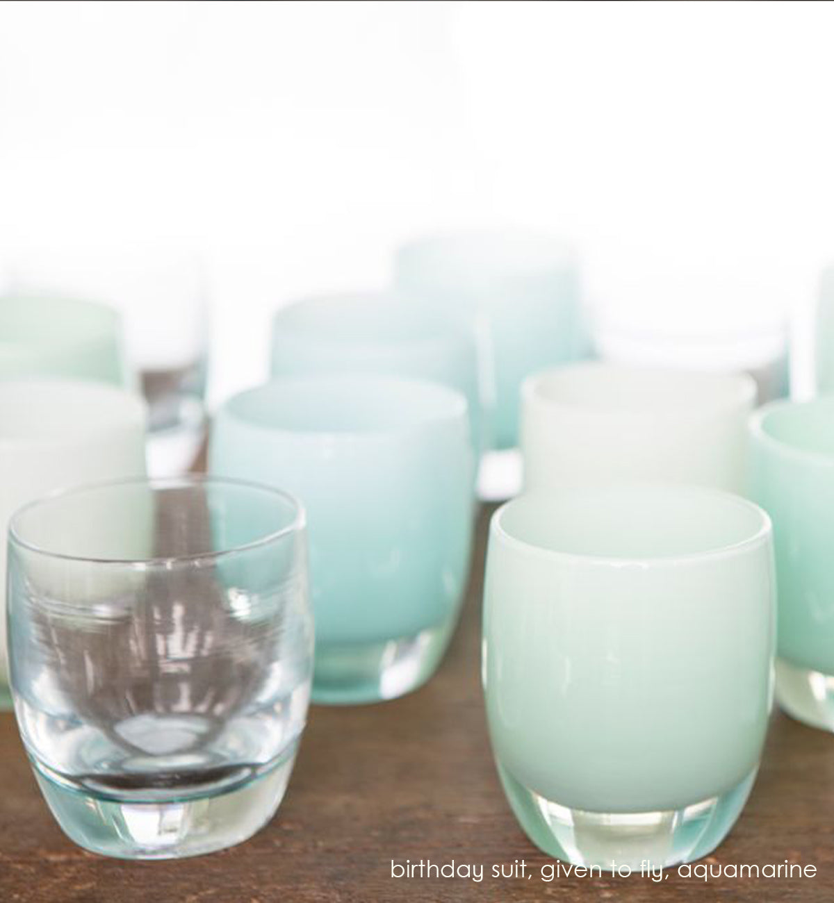 given to fly, sea salt, hand-blown glass votive candle holder on a wood table with birthday suit and aquamarine.