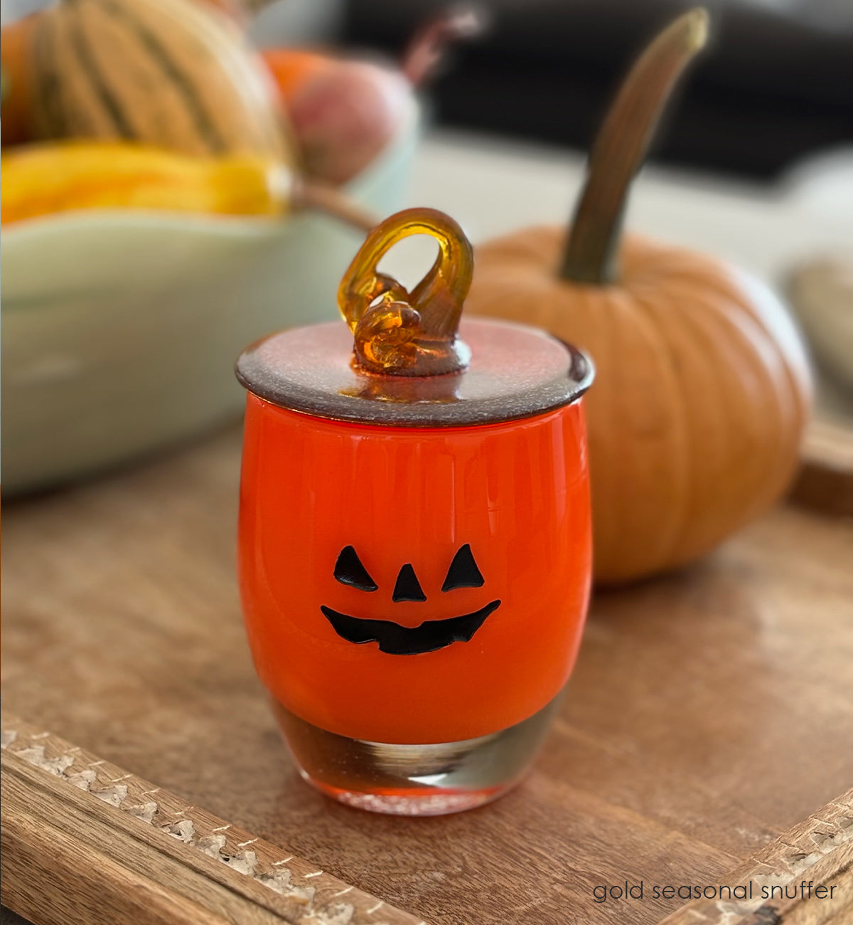 gold seasonal snuffer, gold hand-blown glass votive snuffer in shape of pumpkin top and stem placed on jack-o-lantern on an ottoman tray with gords.