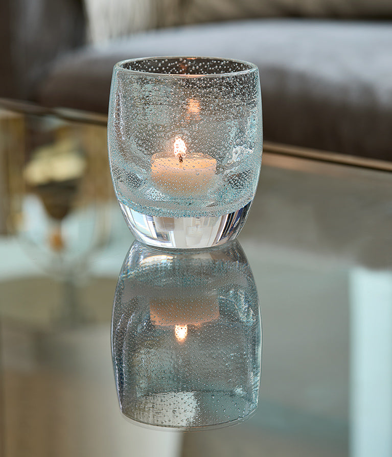 good thoughts, light clear blue with bubbles hand-blown glass votive candle holder on a reflective surface.