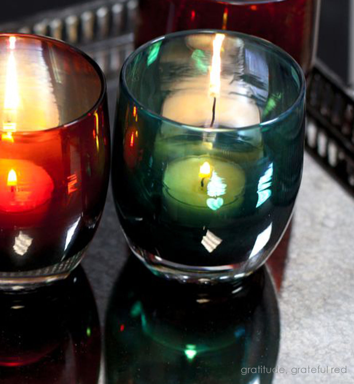 gratitude, textured translucent teal green with silver luster, hand-blown glass votive candle holder lit next to grateful red on a mirrored tray.