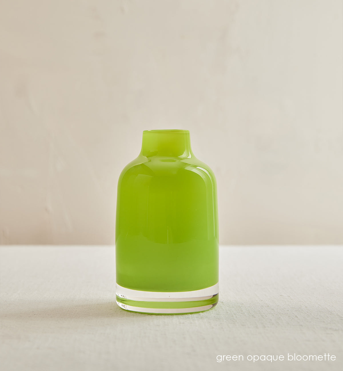 green opaque bloomette, lime green opaque hand-blown glass flower bud vase in front of a cream background.