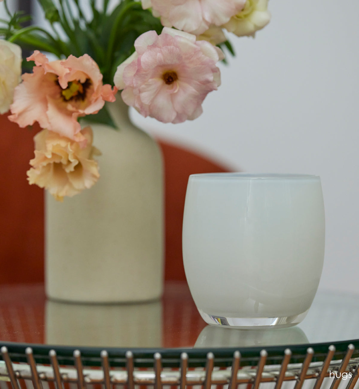 hugs opaque off white hand-blown glass votive candle holder on a table with a white ceramic vase.