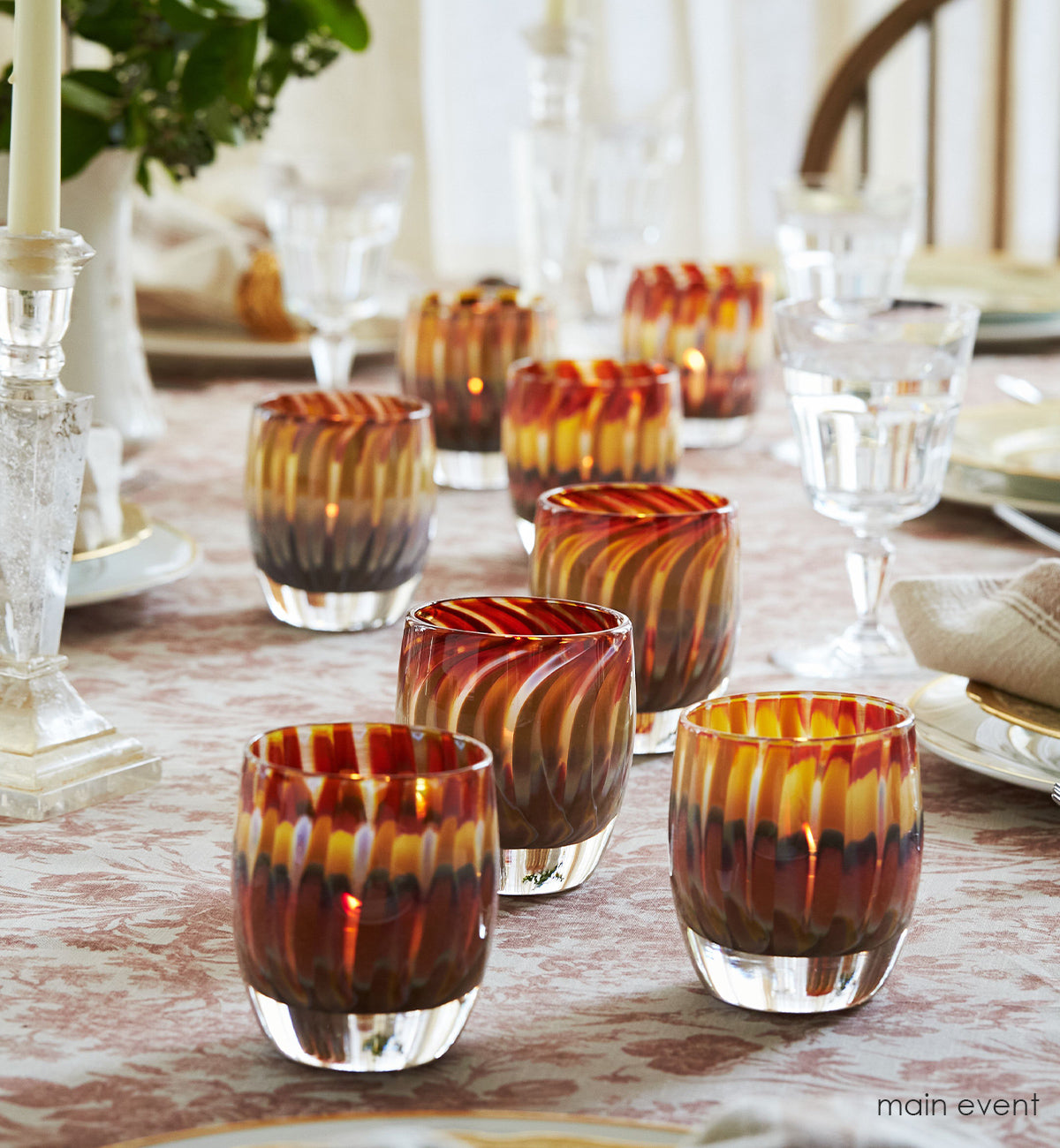 several main event, multi-colored red, brown, cream, yellow raked hand-blown glass votive candle holders on a set dining room table