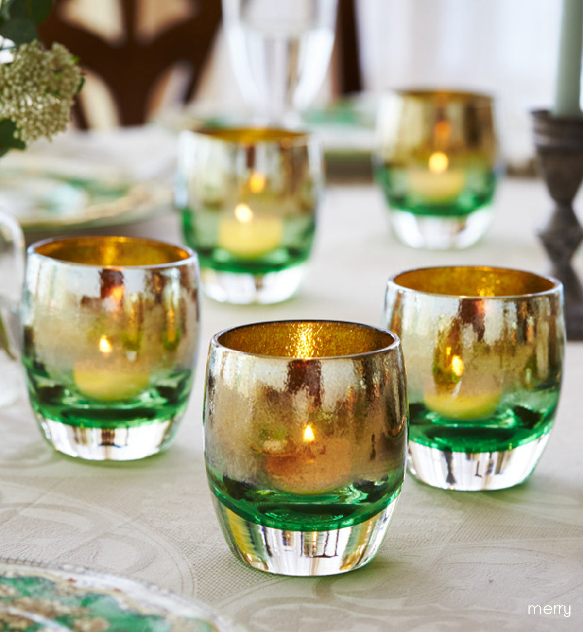 grouping of merry, green with gold shimmer hand-blown glass votives on a set dining room table.