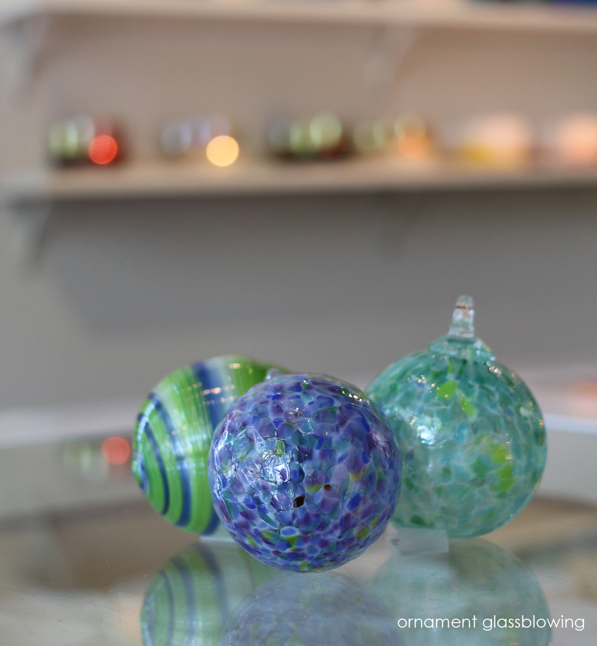 three glassybaby ornaments in variety in blue and green and white shades, hand-blown glass ornaments on a glassybaby retail shop counter.