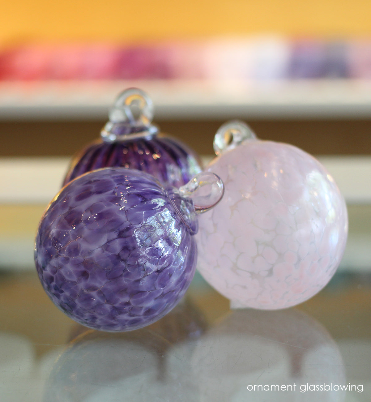 three glassybaby ornaments in varying purples and pink, hand-blown glass ornaments on a glassybaby retail shop counter.