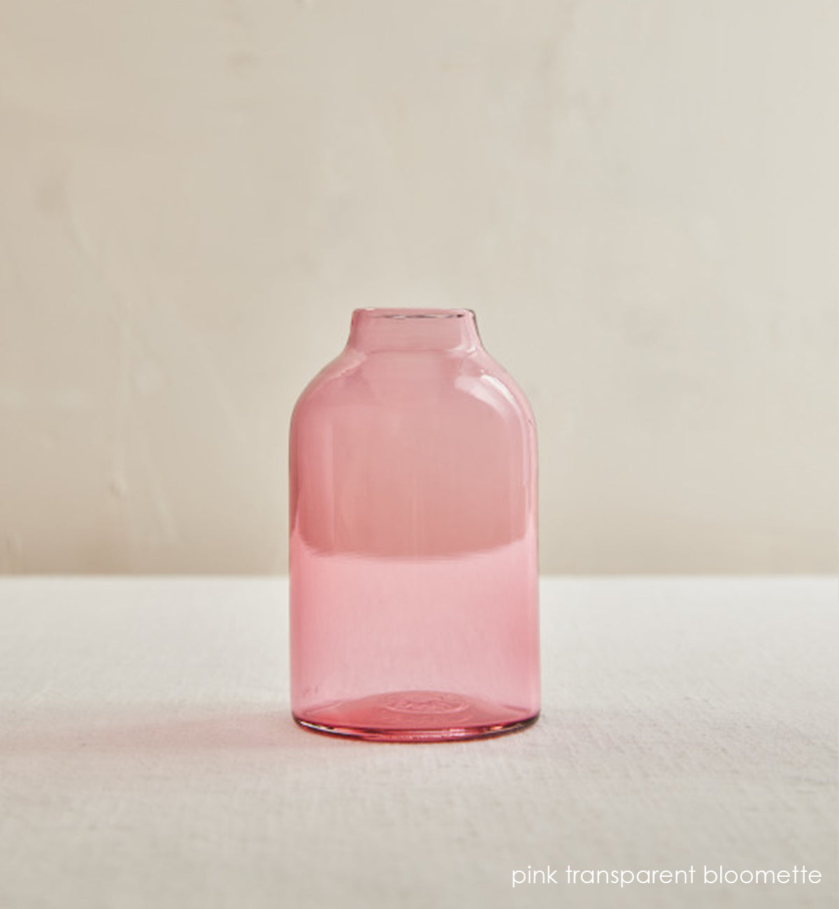 pink transparent bloomette, pink transparent hand-blown glass flower bud vase in an interior cream setting.