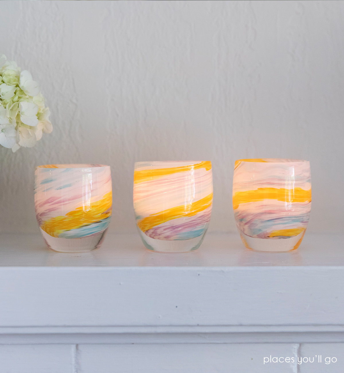 three places you'll go multi-colored swirl hand-blown glass votive candle holders placed on a white mantle next to flowers.