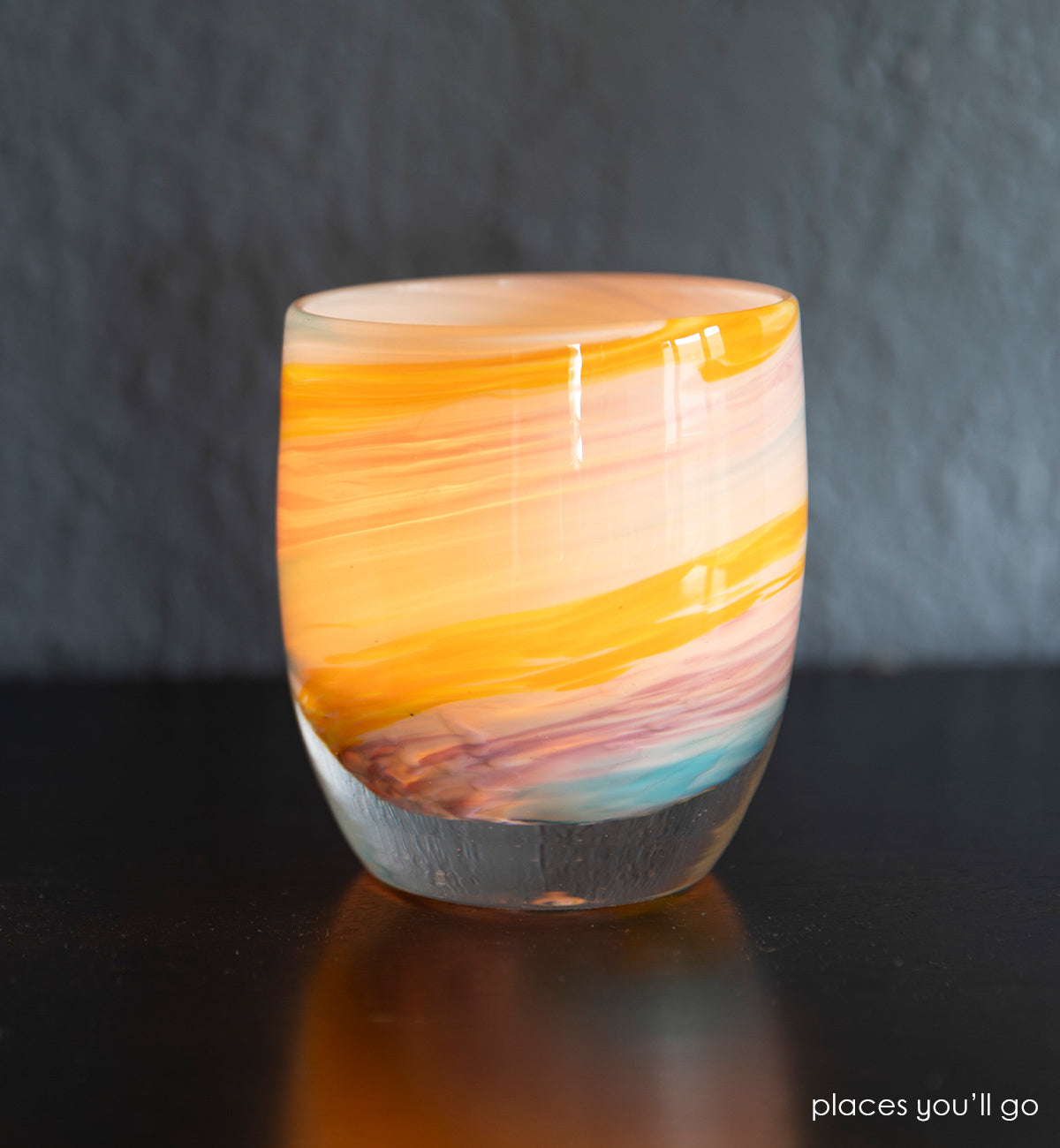 places you'll go hand-blown multi-colored yellow, white, blue, purple swirl hand-blown glass votive candle holder set on a dark brown wood table with a white wall background.