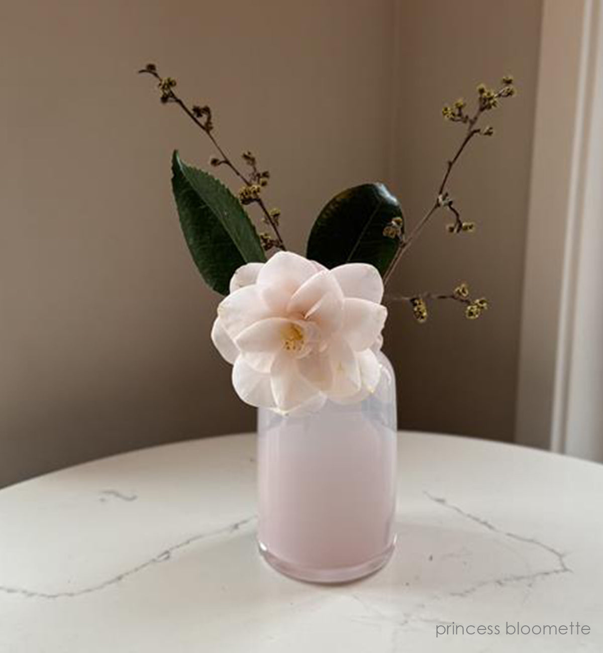 'priness bloomette'  light pink opaque hand-blown glass flower bud vase holding pink flower on white and grey marble table. 