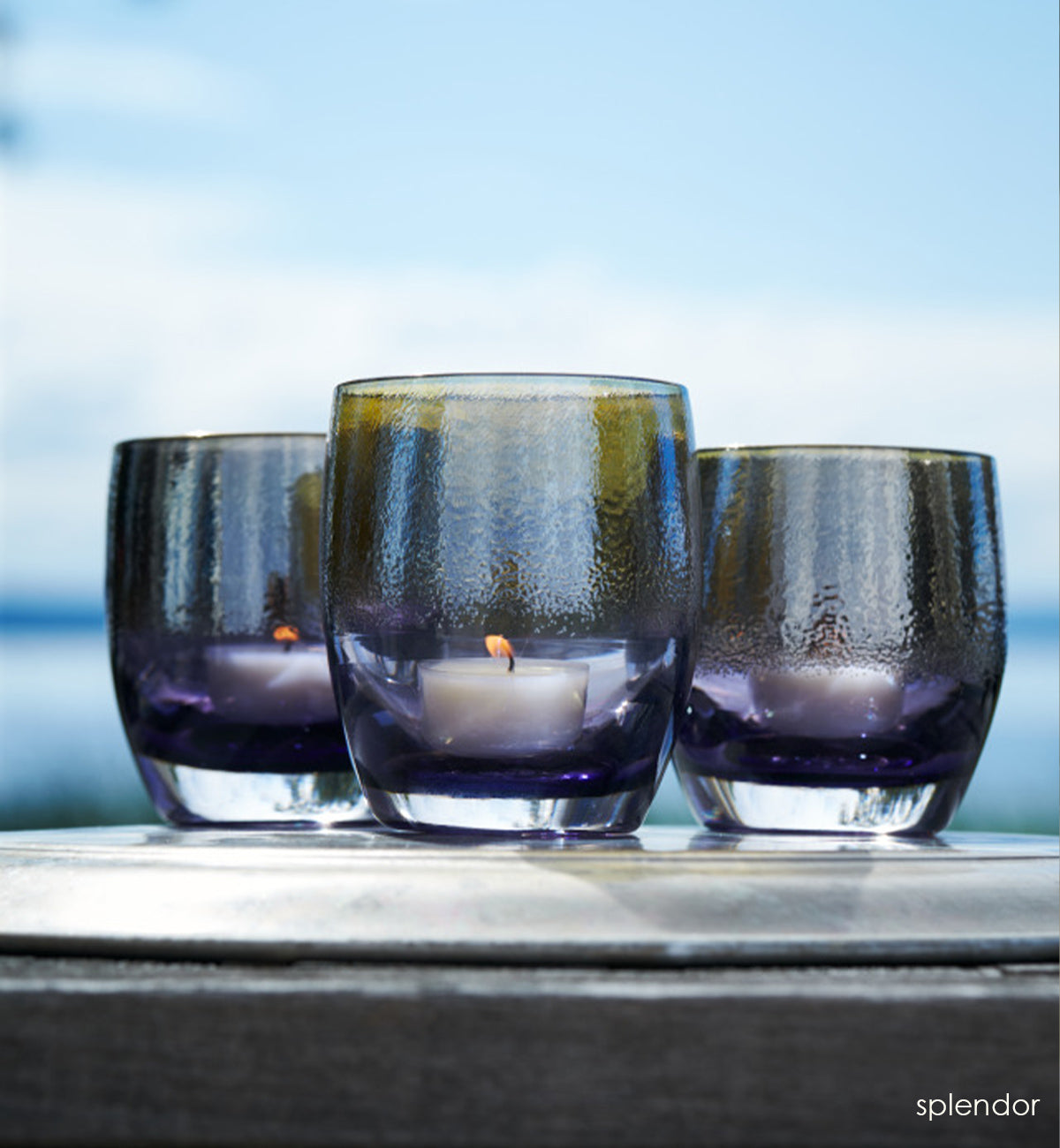 three splendor, purple with silver shimmer hand-blown glass votive candle holders sitting outside with Puget Sound in the background.