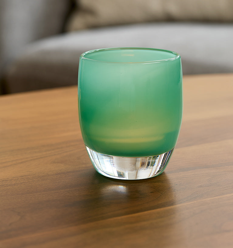 strength,  teal green hand-blown glass votive candle holder on a wood coffee table.