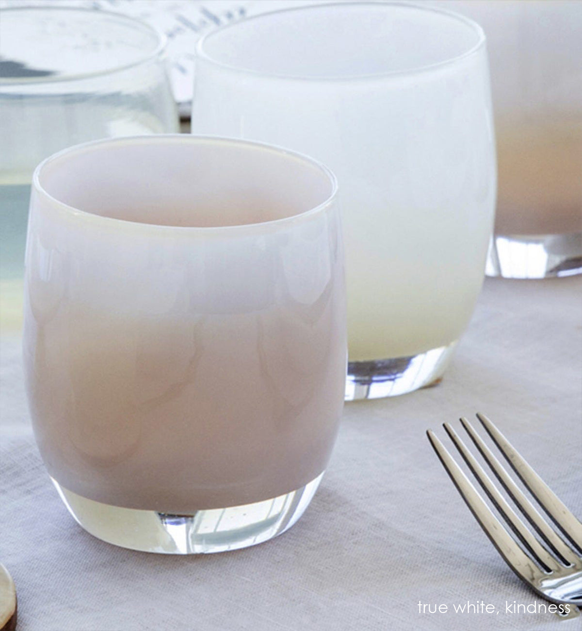 true white, opaque pinky white, hand-blown glass votive candle holder next to kindness and a fork on a dining table.