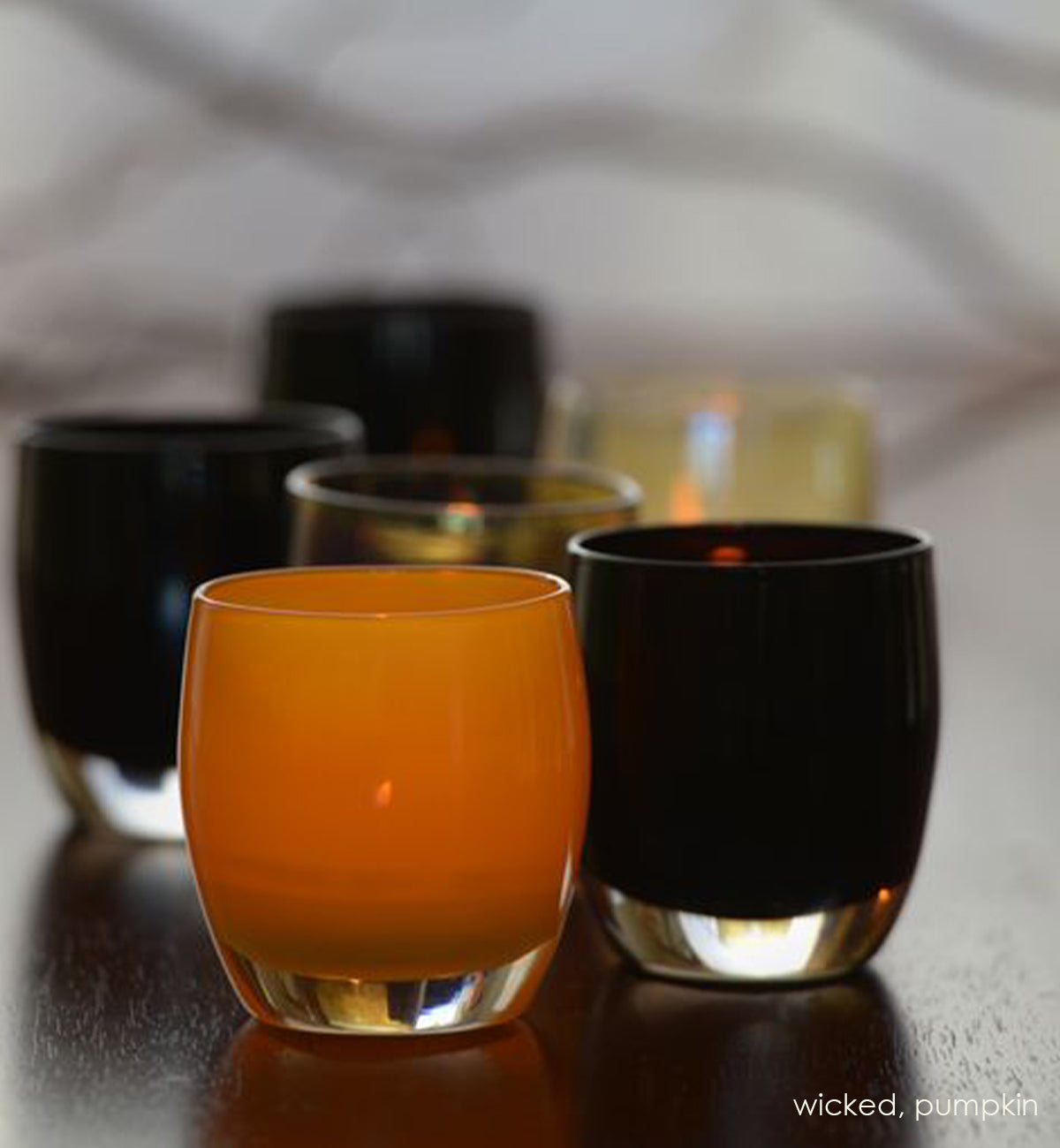 several wicked, opaque purple black, hand-blown glass votive candle holders with pumpkin on a dark wood table.