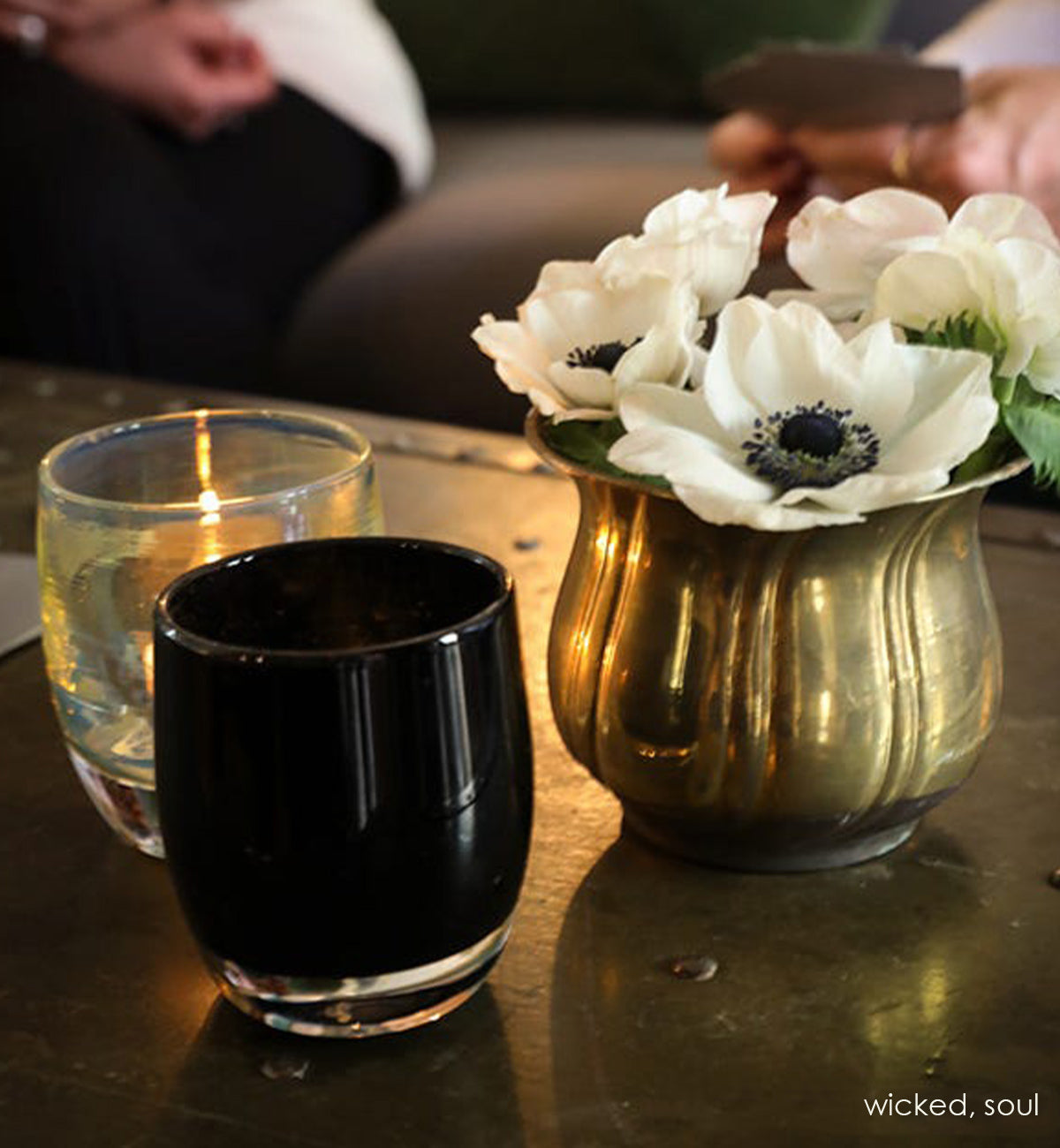 wicked, opaque purple black, hand-blown glass votive candle holder with soul on a coffee table with a vase of flowers.